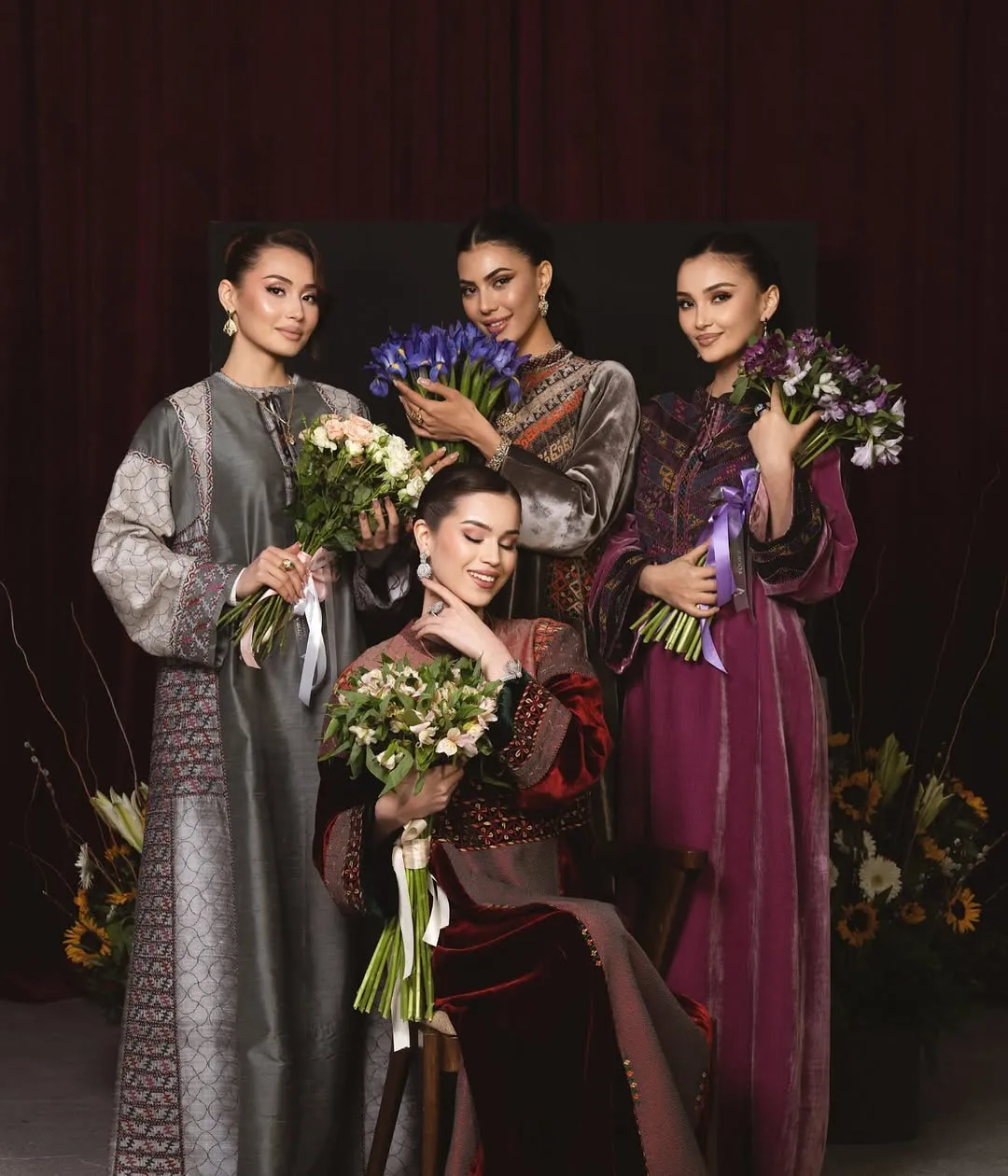 Four models in couture robes before burgundy velvet — campaign portrait with floral bouquets